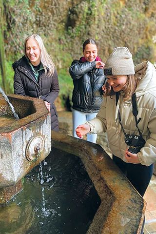 Three young women standing by fountain