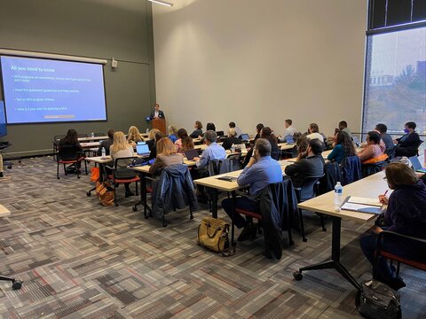 Small crowd of workshop attendees sit in a room 