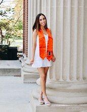 Smiling young woman in white dress and orange graduation stole 