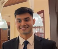 Smiling, dark haired man in suit poses indoors