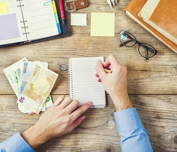 Mix of office supplies, gadgets, and money on a wooden table background