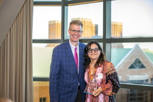 Woman holding award poses for picture with man in front of window